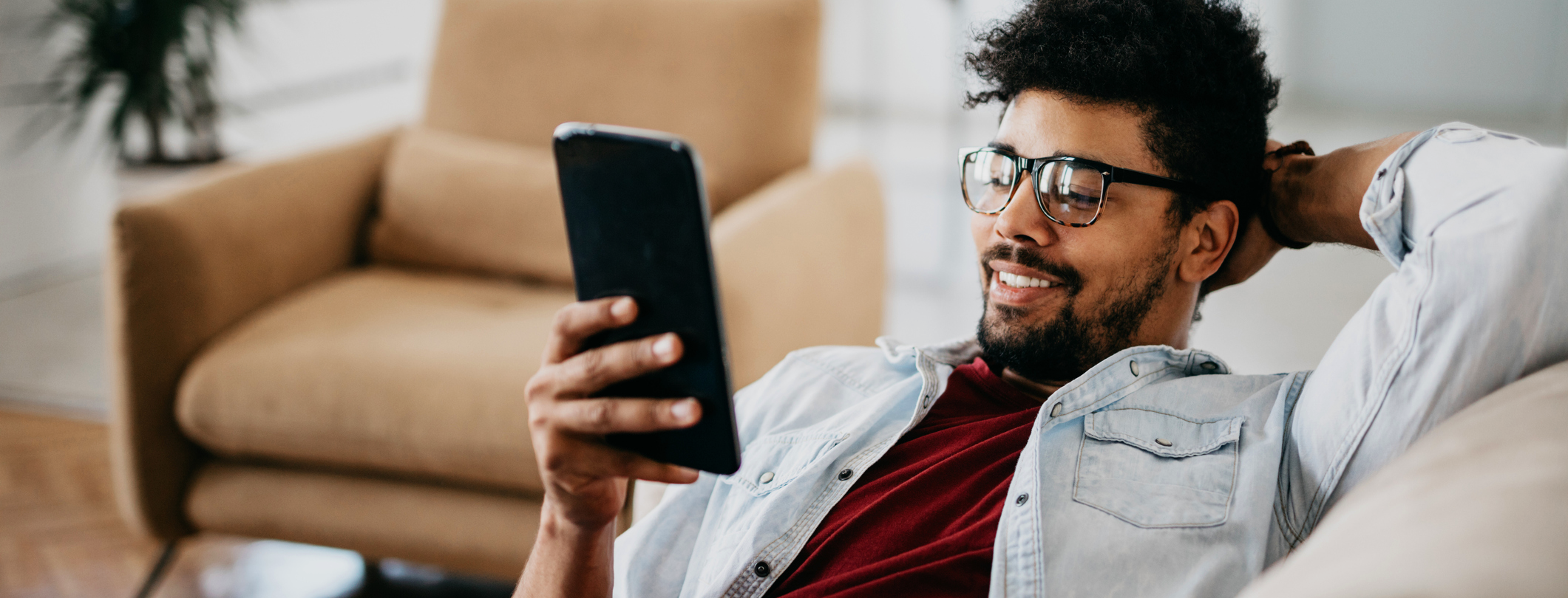 man with glasses with hand behind head looking at large mobile phone