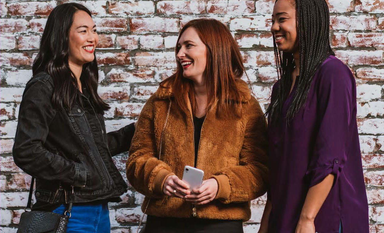 three women stand together with phone