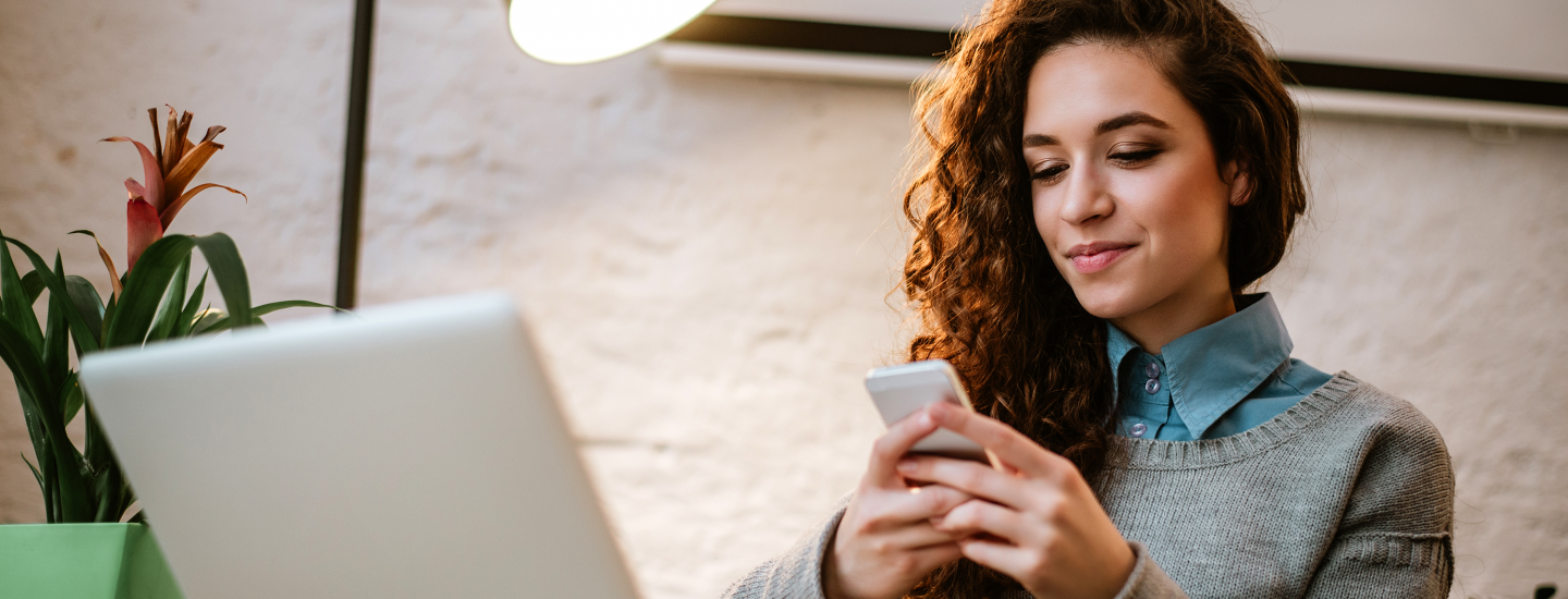 girl looking at cell in front of open laptop