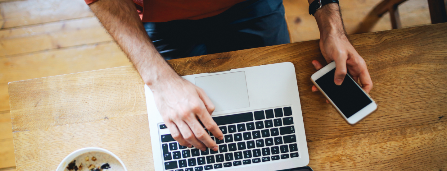man holding cell phone and typing on laptop