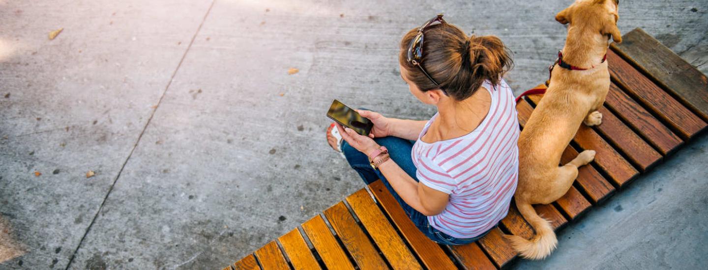 Woman sitting with a dog on a bench outside using her cell phone