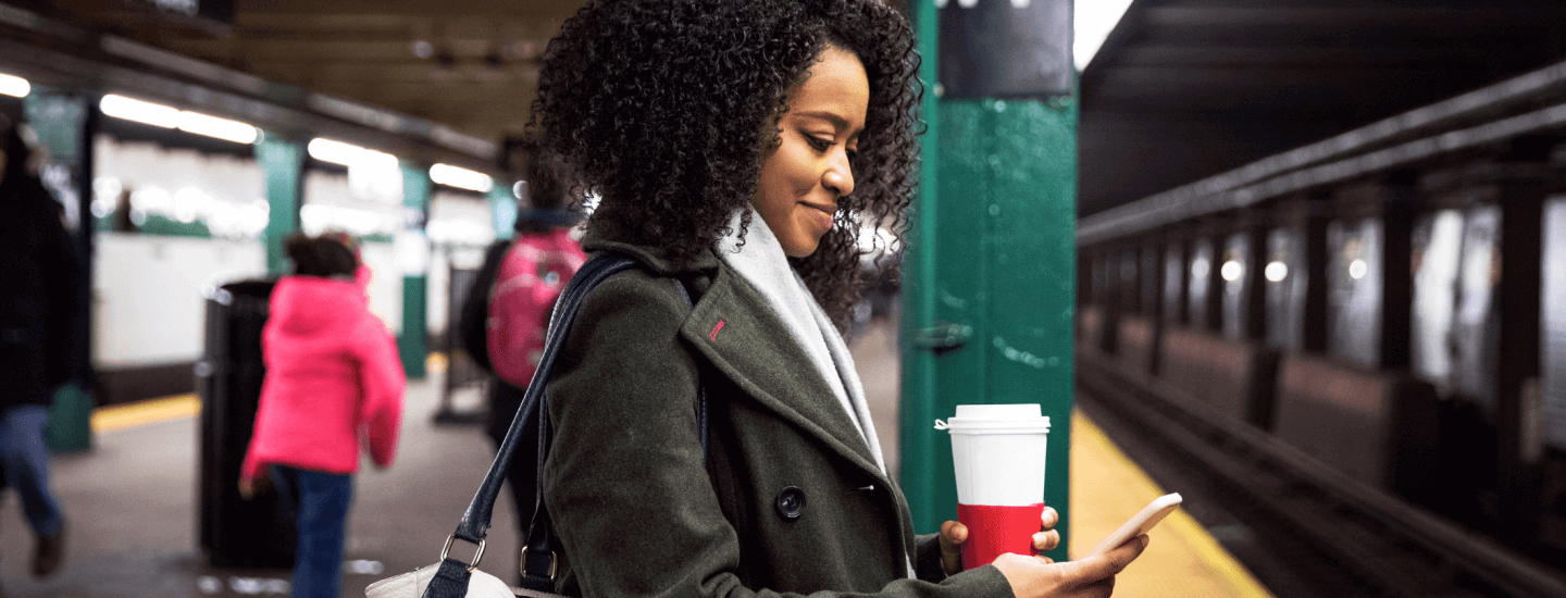 Woman at the subway having coffee and looking at phone.