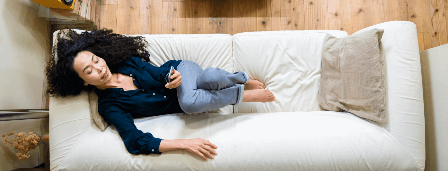 Woman on her phone while laying on couch.