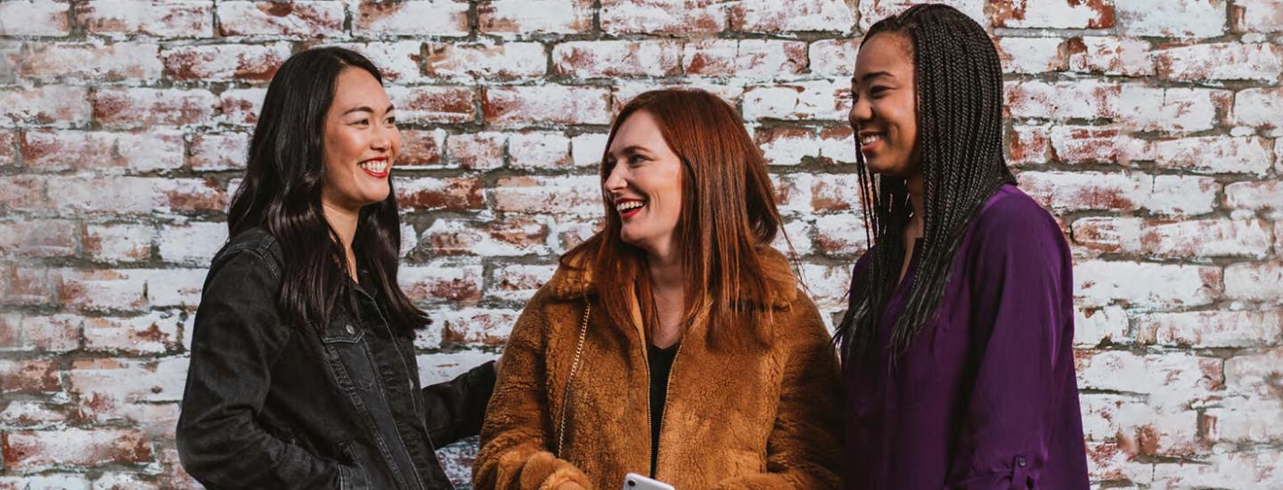 Three women stand together against brick wall