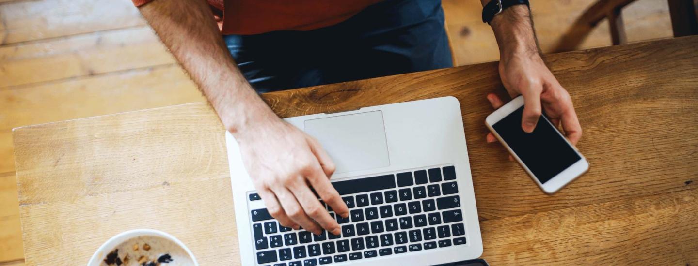 Man uses phone and laptop at table