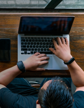 man typing on laptop on wood table