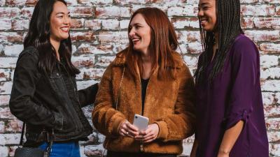 three women stand together with phone